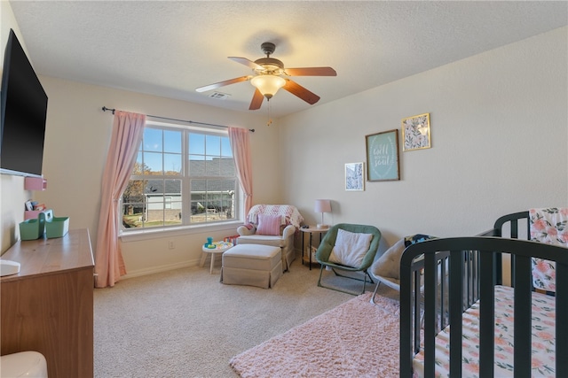 bedroom featuring ceiling fan, carpet, a nursery area, and a textured ceiling