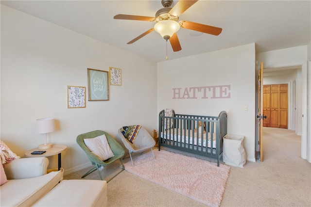 bedroom with carpet, ceiling fan, and a crib