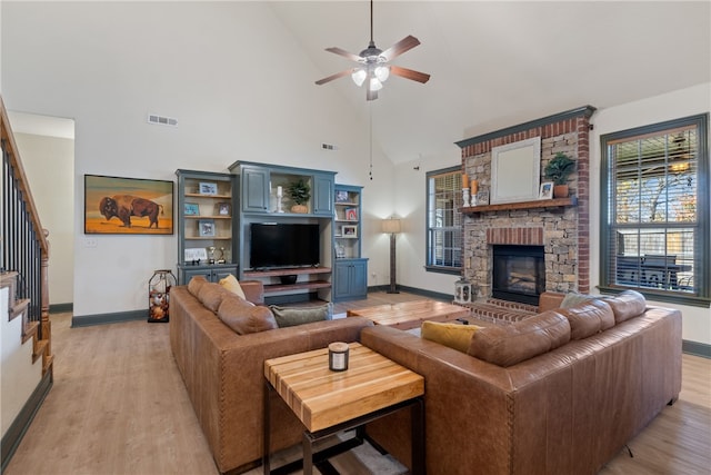 living room featuring ceiling fan, a stone fireplace, high vaulted ceiling, and light hardwood / wood-style flooring