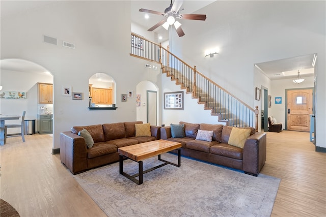 living room featuring ceiling fan, a towering ceiling, and light hardwood / wood-style floors