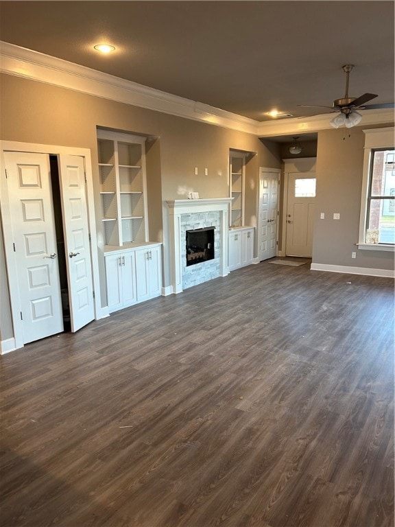 unfurnished living room with a stone fireplace, ceiling fan, dark hardwood / wood-style floors, built in shelves, and ornamental molding