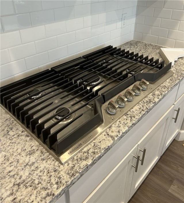 room details featuring dark hardwood / wood-style flooring, backsplash, light stone counters, stainless steel gas cooktop, and white cabinets