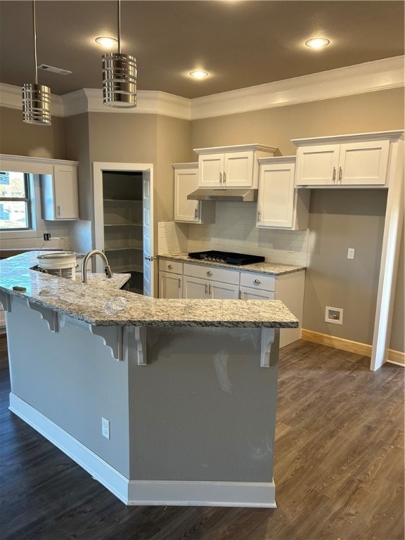 kitchen featuring light stone counters, a kitchen bar, a kitchen island with sink, white cabinets, and ornamental molding