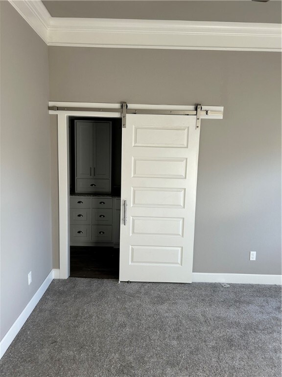 unfurnished bedroom with dark colored carpet, a barn door, and crown molding