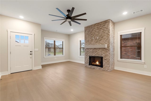 unfurnished living room with baseboards, ceiling fan, light wood-style flooring, visible vents, and a fireplace