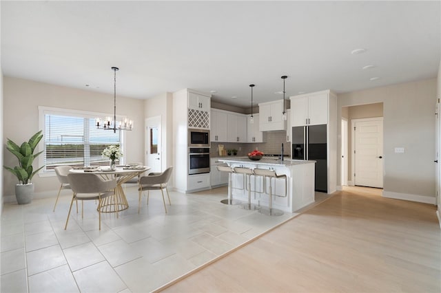 kitchen with a notable chandelier, white cabinetry, a breakfast bar area, appliances with stainless steel finishes, and decorative backsplash