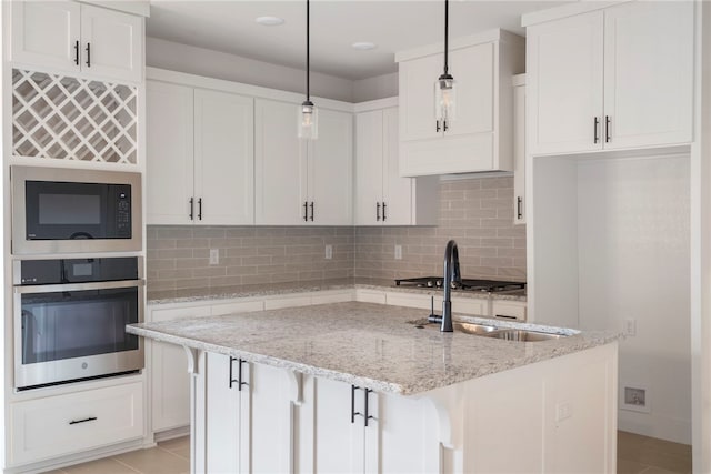 kitchen featuring stainless steel oven, backsplash, built in microwave, a kitchen island with sink, and white cabinets