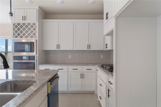 kitchen with stainless steel appliances, white cabinetry, a sink, backsplash, and light tile patterned floors