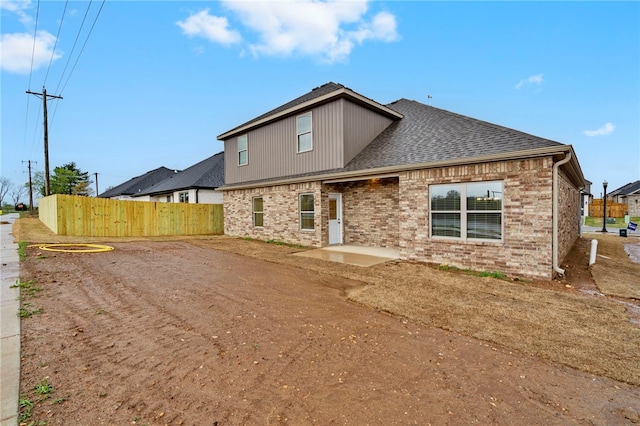 back of house with brick siding, a shingled roof, and fence