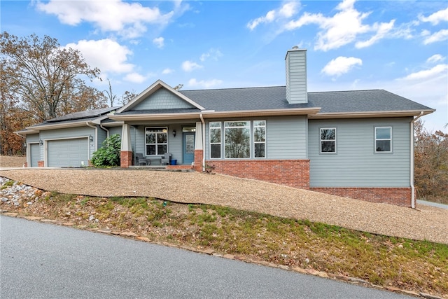 view of front of home with a shingled roof, a chimney, an attached garage, roof mounted solar panels, and brick siding