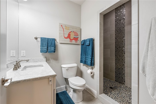 bathroom with baseboards, tiled shower, vanity, and toilet