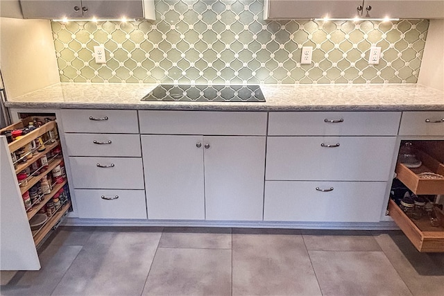 kitchen with light stone counters, dark tile patterned floors, black electric cooktop, and white cabinetry