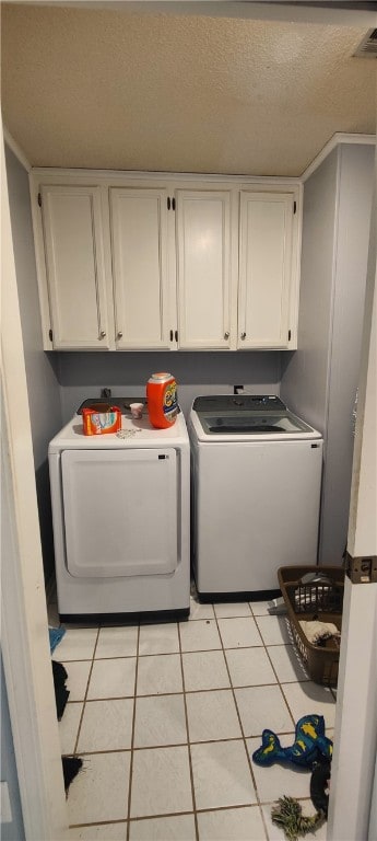 laundry area featuring cabinets, light tile patterned floors, a textured ceiling, and washer and clothes dryer