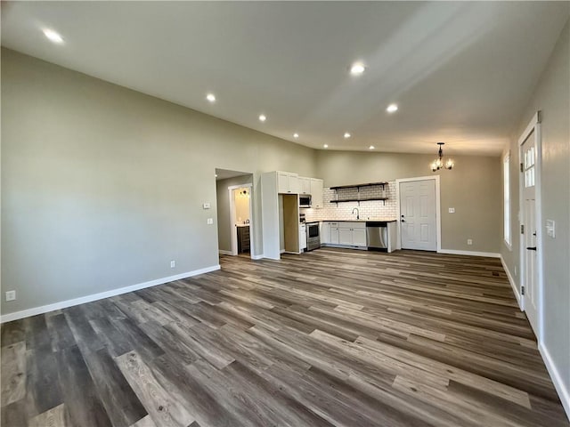 unfurnished living room featuring vaulted ceiling, dark hardwood / wood-style floors, and an inviting chandelier