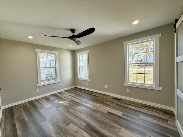 spare room featuring a barn door, ceiling fan, and dark hardwood / wood-style flooring