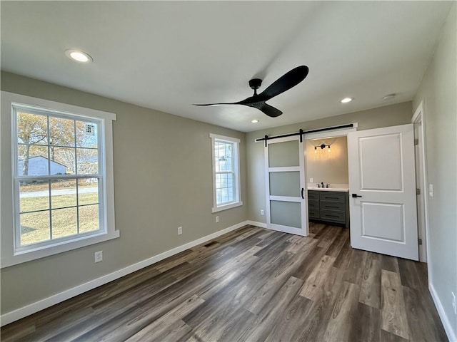 unfurnished bedroom featuring hardwood / wood-style floors, sink, ensuite bath, ceiling fan, and a barn door