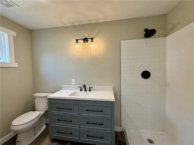 bathroom featuring a tile shower, vanity, wood-type flooring, and toilet