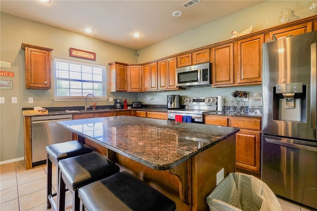 kitchen with a center island, a kitchen breakfast bar, sink, light tile patterned floors, and stainless steel appliances