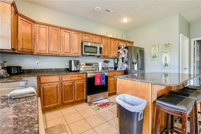 kitchen featuring a breakfast bar, sink, light tile patterned floors, appliances with stainless steel finishes, and a kitchen island