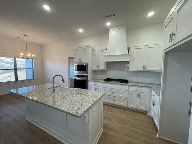 kitchen with decorative light fixtures, white cabinetry, custom range hood, and appliances with stainless steel finishes