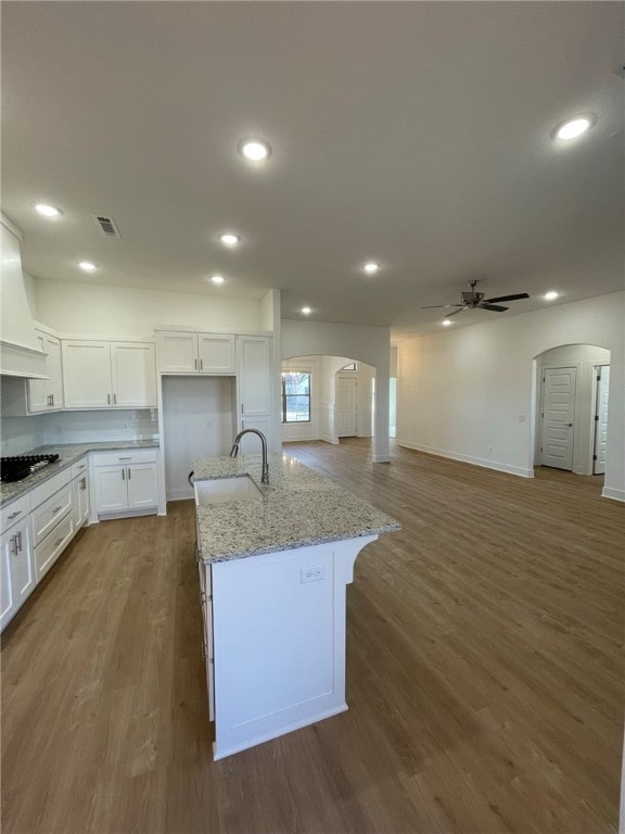 kitchen featuring light stone countertops, dark hardwood / wood-style flooring, sink, a center island with sink, and white cabinets