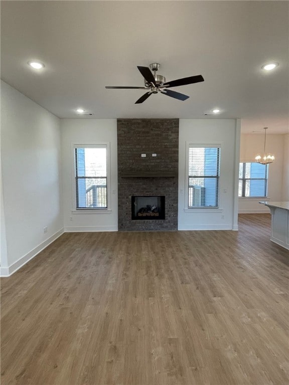 unfurnished living room featuring a fireplace, light wood-type flooring, and ceiling fan with notable chandelier