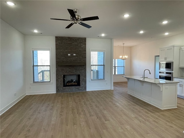 kitchen with white cabinets, light stone counters, stainless steel appliances, and an island with sink