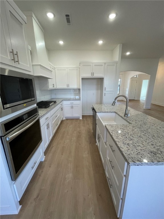 kitchen with white cabinetry, custom exhaust hood, stainless steel appliances, and light hardwood / wood-style floors