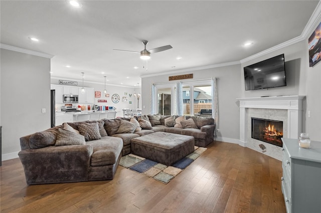 living room with a fireplace, dark wood-type flooring, ceiling fan with notable chandelier, and ornamental molding