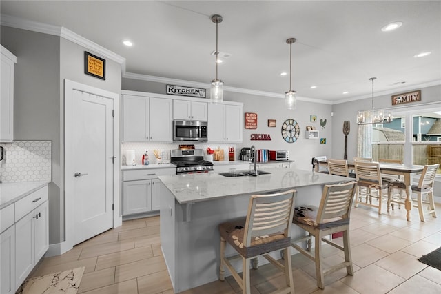 kitchen featuring white cabinetry, sink, hanging light fixtures, stainless steel appliances, and a center island with sink