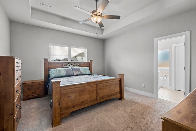 carpeted bedroom with ceiling fan, a tray ceiling, and ensuite bath