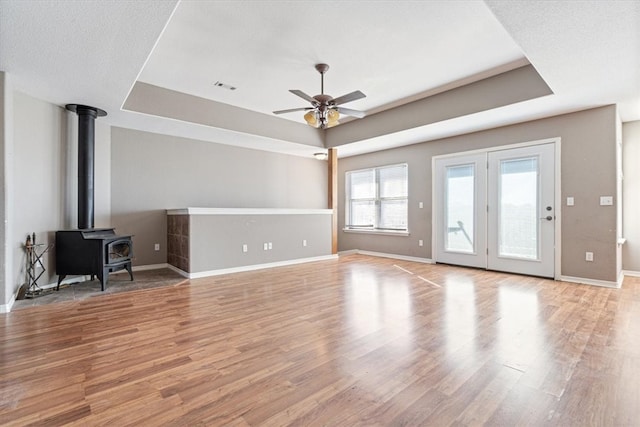 unfurnished living room featuring a tray ceiling, a wood stove, ceiling fan, and light hardwood / wood-style floors