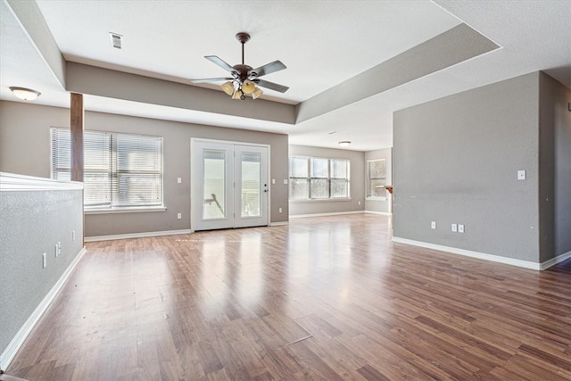 unfurnished living room featuring a tray ceiling, ceiling fan, and hardwood / wood-style floors