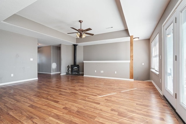 unfurnished living room featuring a wood stove, ceiling fan, and light hardwood / wood-style flooring