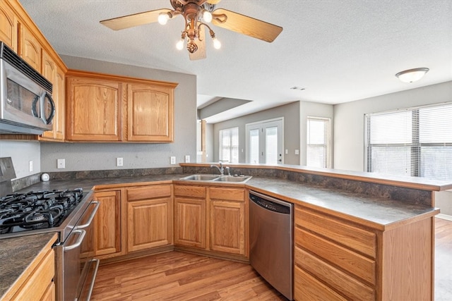 kitchen with sink, stainless steel appliances, kitchen peninsula, light hardwood / wood-style floors, and a textured ceiling