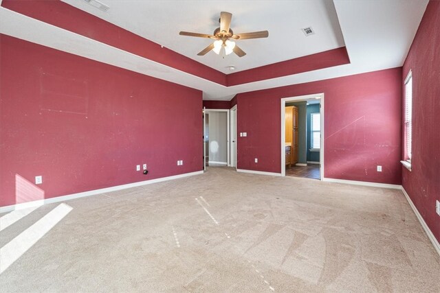 unfurnished bedroom with ceiling fan, a raised ceiling, and light carpet