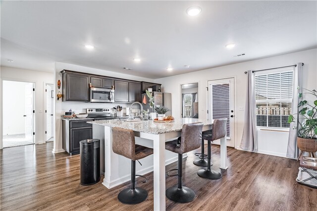 kitchen featuring a breakfast bar, a kitchen island with sink, dark wood-type flooring, appliances with stainless steel finishes, and dark brown cabinets