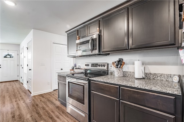 kitchen featuring wood-type flooring, dark brown cabinetry, stainless steel appliances, and dark stone counters