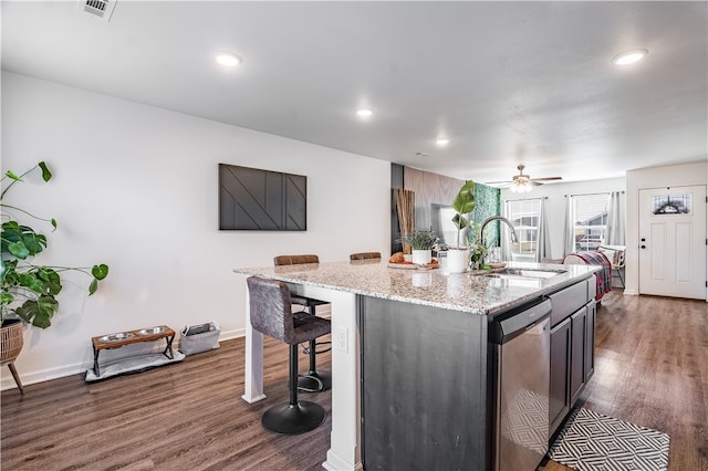 kitchen with light stone countertops, a kitchen island with sink, dishwasher, dark hardwood / wood-style floors, and a breakfast bar area