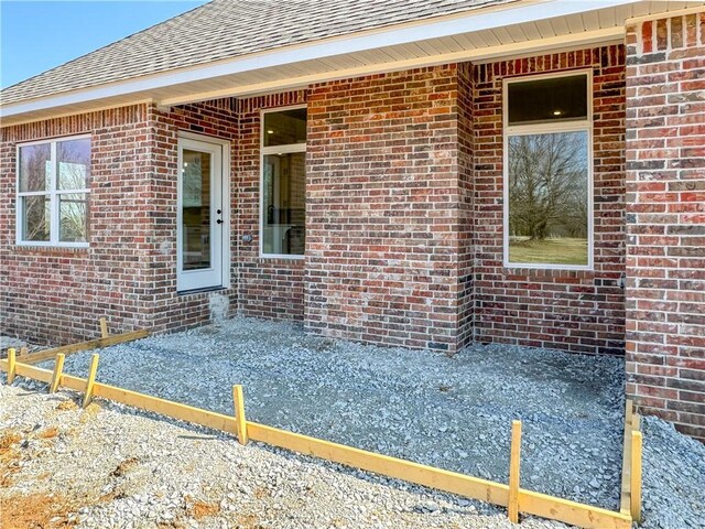 property entrance with a shingled roof and brick siding