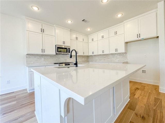 kitchen featuring a center island with sink, stainless steel microwave, and light countertops