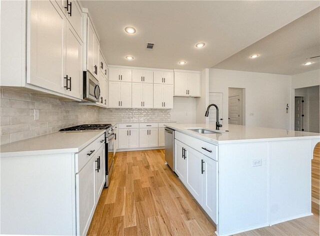 kitchen featuring a center island with sink, white cabinets, appliances with stainless steel finishes, light countertops, and a sink