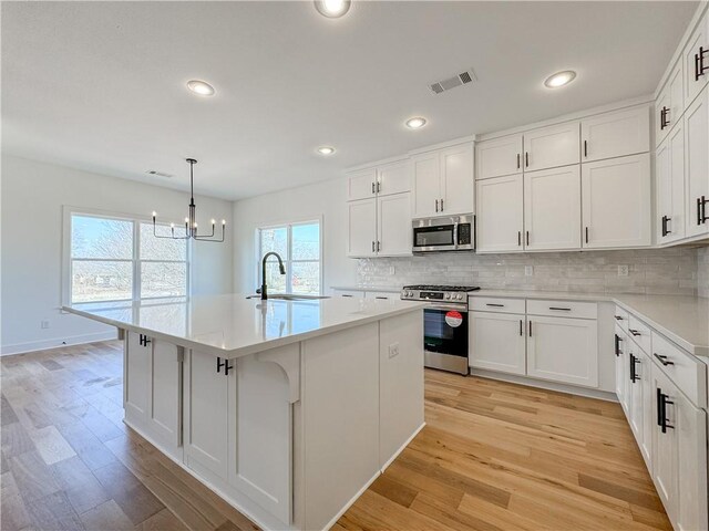 kitchen featuring white cabinets, a center island with sink, stainless steel appliances, and light countertops