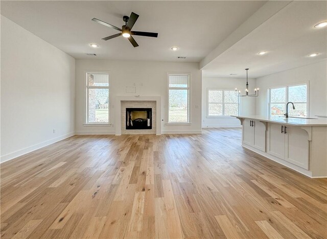 unfurnished living room with light wood-style flooring, a fireplace, baseboards, and ceiling fan with notable chandelier