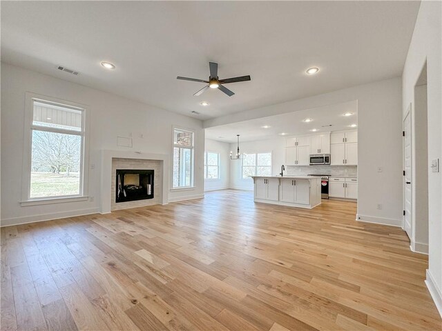 unfurnished living room featuring light wood-type flooring, a fireplace, a sink, and recessed lighting