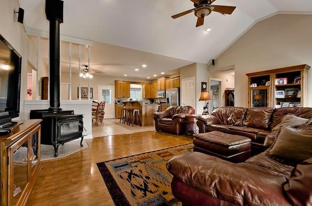 living room featuring a wood stove, ceiling fan, lofted ceiling, and light wood-type flooring