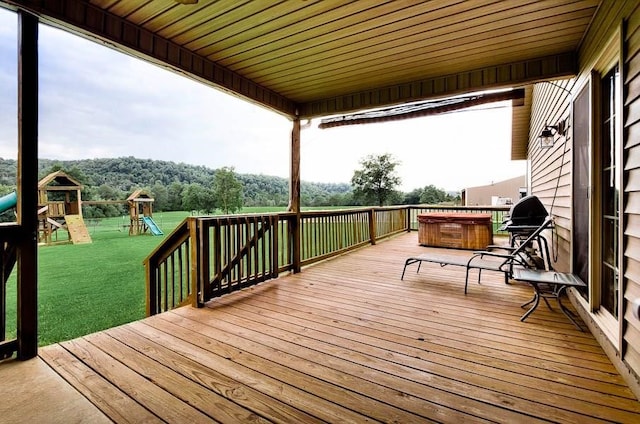 wooden deck featuring a playground, grilling area, a lawn, and a hot tub