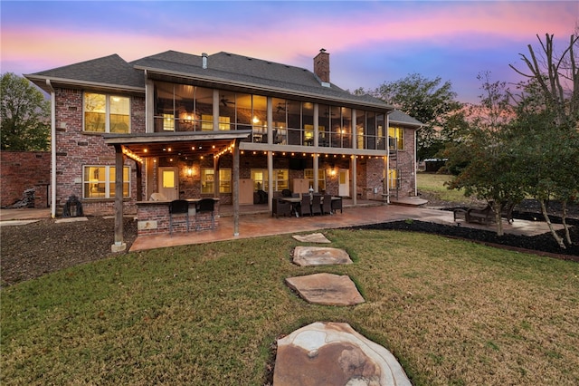 back house at dusk with a lawn, a sunroom, a balcony, and a patio