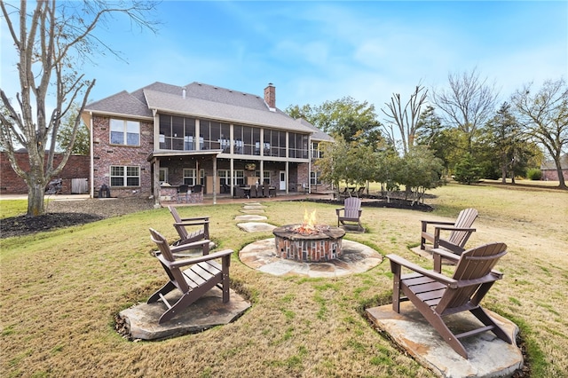 back of house with a sunroom, a patio area, an outdoor fire pit, and a lawn