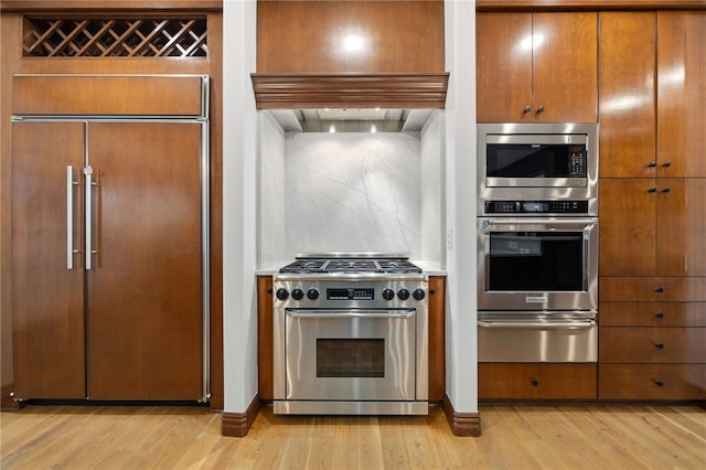 kitchen with high end appliances, backsplash, and light hardwood / wood-style flooring